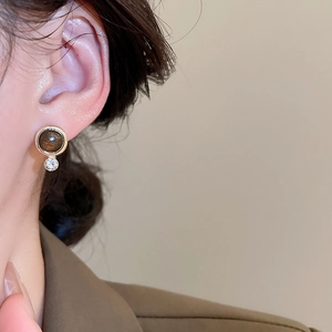 Close-up of vintage geometric tiger eye stud earrings worn with a beige blazer