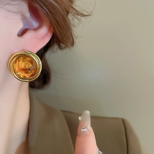 Close-up of amber resin round stud earring with spiral gold metal frame on ear