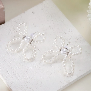 Macro detail of white faux pearl bow earrings on a natural white stone background