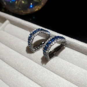 Detail of silver C-shape hoop earrings with blue stones and white zircon on gray velvet