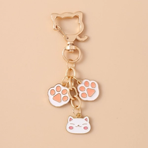 Detail of gold keychain featuring white cat face and pink paw pendants on beige background