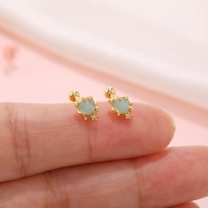 Macro shot of gold marine-style stud earrings with light blue beads on a fingertip