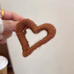 Close-up of a heart-shaped brown plush claw clip held by a hand in soft natural light