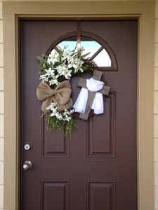 Detail of Easter cross wreath with white lilies and burlap bow on a brown wooden door