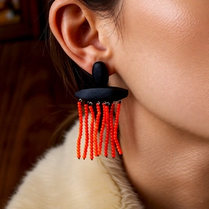 Close-up of oversized ethnic earrings with black wooden top and orange beaded tassels