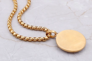 Macro shot of gold-plated praying hands pendant on box chain with marble background