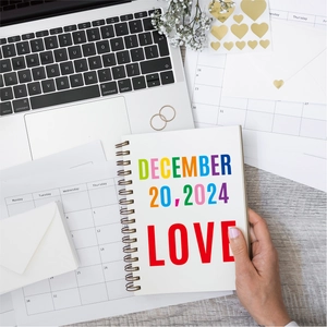 Artistic spiral notebook with colorful 'LOVE' cover held in a cozy desk workspace setting
