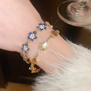 Close-up of a gold shell bracelet and blue enamel flower charm on a model wrist