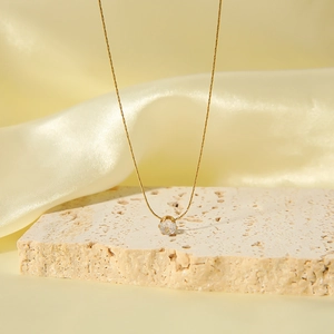 Minimalist gold necklace with a six-prong round zircon pendant on natural stone
