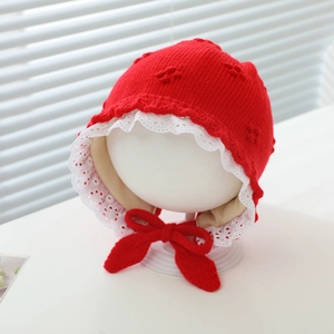 Detailed view of red baby knit bonnet with white lace trim and adjustable bowtie strap