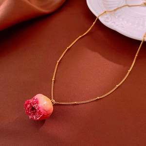 Close-up of a red pomegranate pendant necklace with a gold chain on red fabric