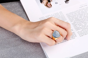 Fashionable golden stainless steel ring with a large blue heart stone on a magazine backdrop