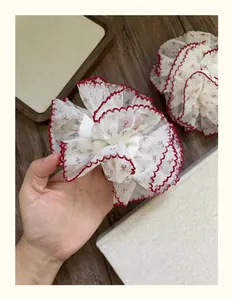Détail d'un chouchou en dentelle blanche avec fleurs rouges et bordure ondulée