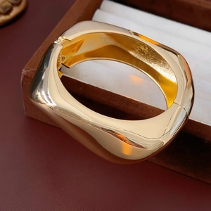 Macro shot of wide gold polished metal bangle featuring a secure hinge closure design