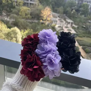 Handmade large fabric flower hair clips in red, purple, and black on a balcony view