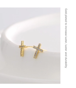 Macro shot of gold plated cross earrings with sparkling cubic zirconia on a white surface