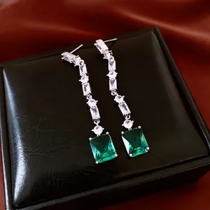 Luxury silver long drop earrings featuring emerald-cut green gemstones on black leather