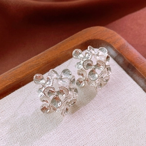 Detailed top view of silver flower stud earrings on white linen and wooden frame