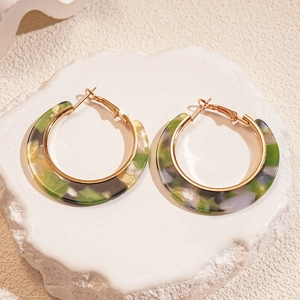 Detail showing C-shaped green and grey acetate earrings with gold metal frames on stone