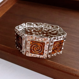 Detail of vintage square enamel bracelet with amber tones and silver metallic swirl patterns