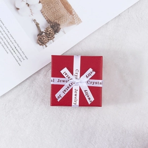 Close-up of red square jewelry gift box with white printed ribbon bow on plush background