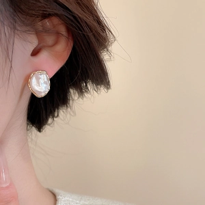 Close-up of pearl stud earrings with golden hammered metal edges on model's ear