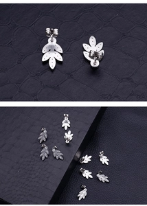 Detailed view of leaf-shaped silver earrings with sparkling crystals on black texture