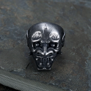 Macro shot of antique silver Hannya mask ring detailing on a textured stone surface