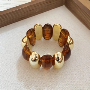Close-up of gold metal beads and dark amber resin beads on an elastic acrylic bracelet