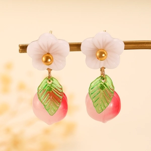 Detail of peach fruit drop earrings with white flower and green leaf accents