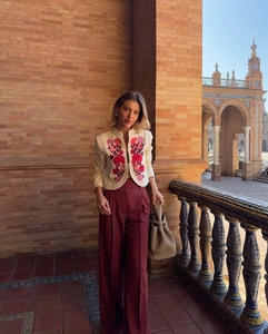 Detail shot of beige cropped jacket with floral embroidery and high-waist burgundy trousers
