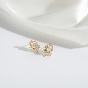 Detail of fan-shaped golden earrings with teardrop zircon on white silk background