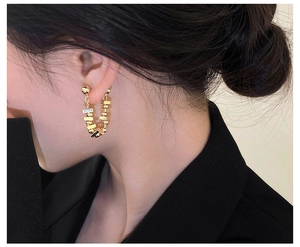 Detail of U-shaped gold chain earrings with geometric beads and sparkling zircon on model