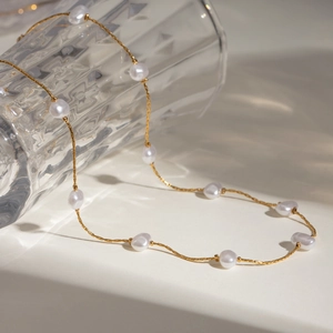 Minimalist gold snake chain necklace with irregular white pearls on a glass cup