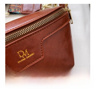 Detail showing the brown litchi grain leather texture and gold logo on the waist bag