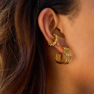 Macro view of gold heart hoop earrings and textured ear cuff set on model's ear