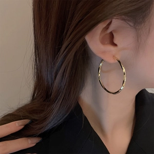 Close-up of golden twisted hoop earrings worn to show style and large size scale