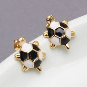 Macro view of gold turtle earrings with black and white soccer pattern on ceramic surface