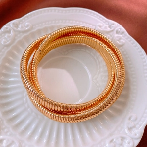 Détail d'un bracelet serpent doré multi-rangs posé sur une assiette en céramique en relief