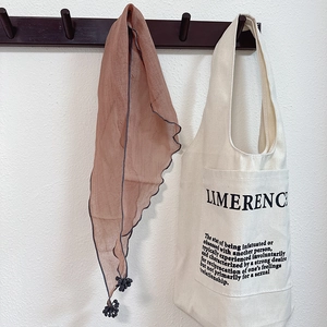Brown tassel scarf with wavy edges hanging on a beige canvas tote bag with text