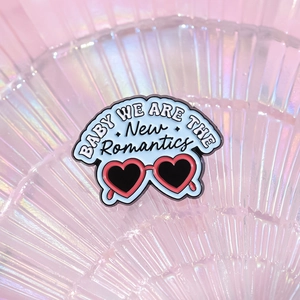Enamel brooch with heart sunglasses design and New Romantics slogan on pink background