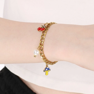 Gros plan d'un bracelet doré avec champignon en émail, cerise et perle sur un poignet
