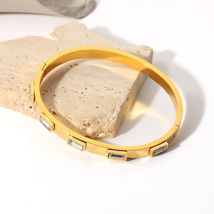 Détail d'un bracelet en acier titane doré avec zircons rectangulaires sur socle en pierre