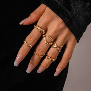 Close-up of 6 gold geometric rings with irregular textures worn on a model's hand