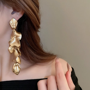 Detail of model wearing long gold layered petal tassel earrings with a matte brushed finish