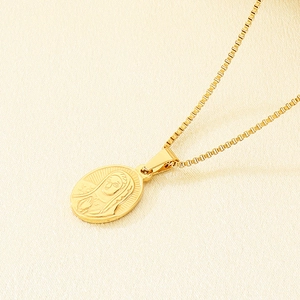 Detailed 45-degree angle of a gold religious oval portrait pendant on textured fabric