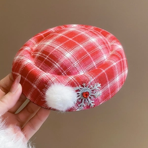 Close-up of red plaid beret with a fluffy white pompom and silver snowflake brooch