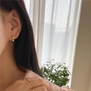 Detail of elegant gold twist pearl earrings and wavy ring worn by a model