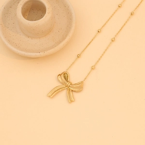 Detailed close-up of golden bow pendant necklace with beaded chain on beige background