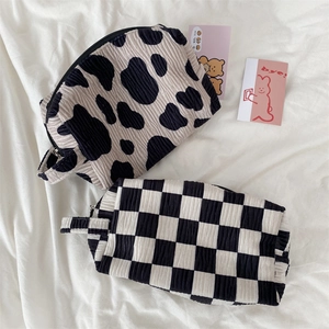 Detail of corduroy cow print and checkerboard makeup bags with black handles and metal zippers